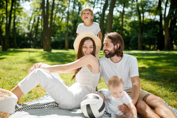 Des parents joyeux et leur fils et leur petite fille, vêtus de vêtements blancs, se reposent sur le pique-nique dans le parc. Famille heureuse . — Photo
