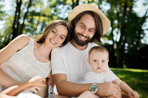 Jeune mère brune et père vêtus de vêtements blancs tiennent dans les bras petite fille charmante et souriante . — Photo