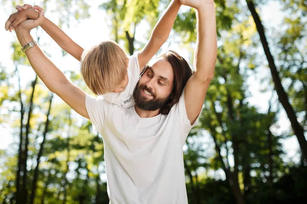 Pai com seu filhinho estão vestidos com as camisetas brancas. Eles estão brincando ao ar livre com rostos felizes . — Fotografia de Stock