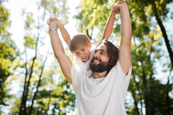 Il padre con il suo figlioletto e 'vestito con le magliette bianche. Stanno giocando all'aperto con facce felici . — Foto Stock