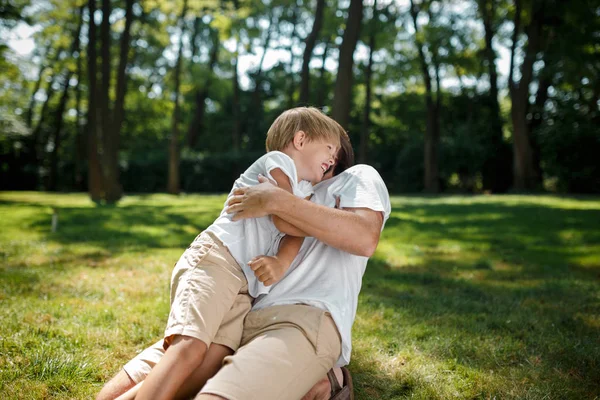 Kleiner blonder Junge und sein Vater amüsieren sich und lachen auf dem grünen frischen Gras unter freiem Himmel. — Stockfoto