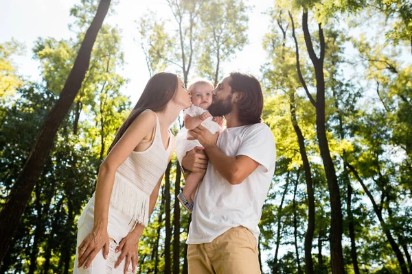 Glückliche Familie an der frischen Luft. junge dunkelhaarige Frau und ihr Mann küssen ihre charmante kleine Tochter. — Stockfoto