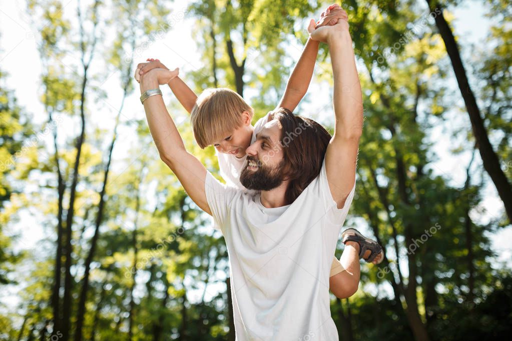 Father with his little son are dressed in the white t shirts. They are fooling around outdoor with happy faces.