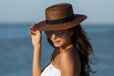 Beyaz elbise, güneş gözlüğü ve şapka güneşli bir deniz kenarında güzel esmer kız portresi.