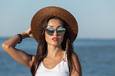 Uzun saç ve kırmızı ruj beyaz elbise, güneş gözlüğü ve kahverengi şapka deniz kenarında muhteşem bir esmer kız portresi