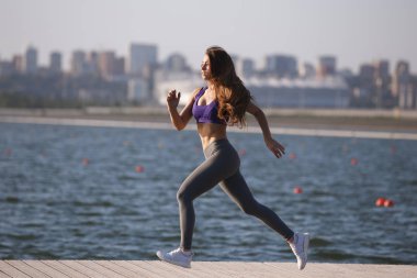 Uzun kahverengi saçlı bir spor üniforma giymiş güzel genç kız yaz gününde ahşap iskele üzerinde çalışıyor .