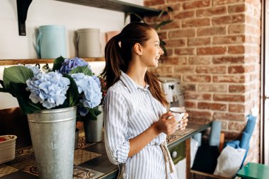 Çizgili bir elbise giymiş güzel esmer kız çiçek dükkan ışık mavi HORTENSIA ile vazo yakın duruyor ve bir fincan tutar