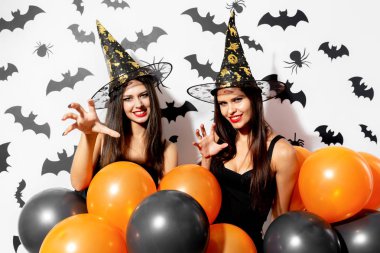 Cadı şapkaları büyüleyici genç kadınlarda iki siyah yarasalar ile beyaz bir arka plan üzerinde siyah ve turuncu balonlarla vardır. Cadılar Bayramı