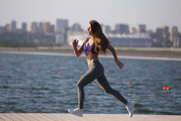 Mooi jong meisje met lang bruin haar, gekleed in een uniform sport draait op de houten pier op de zomerdag . — Stockfoto