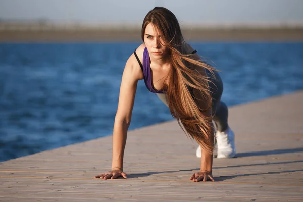 Schönes junges Mädchen mit langen braunen Haaren in Sportkleidung beim Planken auf dem Holzsteg am Wasser an einem Sommertag — Stockfoto