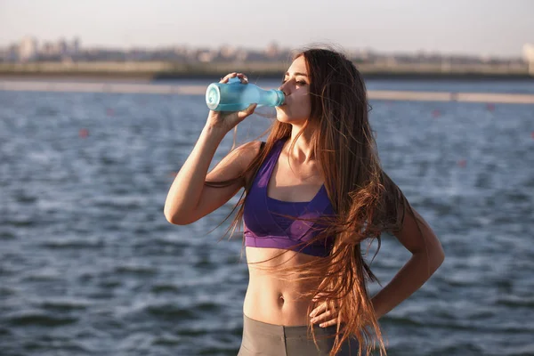 Mooi meisje met lang bruin haar in een sport boven drinkt water op de houten pier — Stockfoto