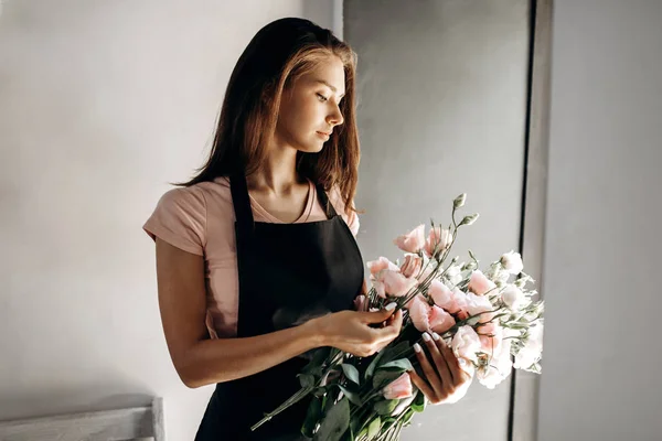 분홍색 t-셔츠와 검은색 앞치마에 젊은 여성 꽃집 파스텔 색상에 eustoms의 꽃다발을 보유 — 스톡 사진