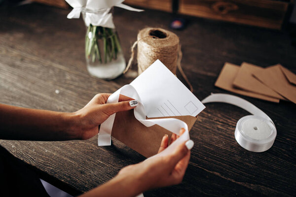 Florist is packing a postcard in an envelope with white ribbon on the wooden table