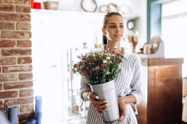 Красива брюнетка, одягнена в смугасту сукню, тримає вазу з рожевими і білими хризантемами в квітковому магазині — стокове фото
