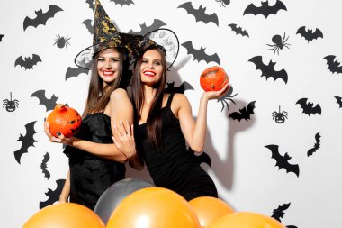 İki esmer kadın cadı şapkaları Halloween pumpkins yarasalar ve örümcekler beyaz bir arka plan üzerinde eğlenin