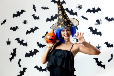 Cadılar Bayramı Balkabağı siyah yarasalar ve örümcekler beyaz bir arka plan üzerinde mavi bir peruk ve witchs şapkalı komik genç kadın tutar