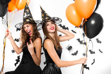 İki esmer kız siyah elbiseler ve cadı şapkaları yarasalar ile duvar arka plan üzerinde balon ile eğlenin. Cadılar Bayramı