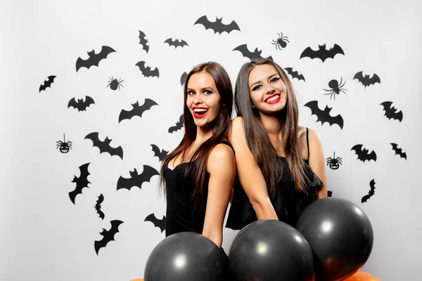 Prachtige brunette vrouw in zwarte jurk houdt zwart en oranje ballonnen op een witte achtergrond met zwarte vleermuizen en spinnen. Halloween — Stockfoto