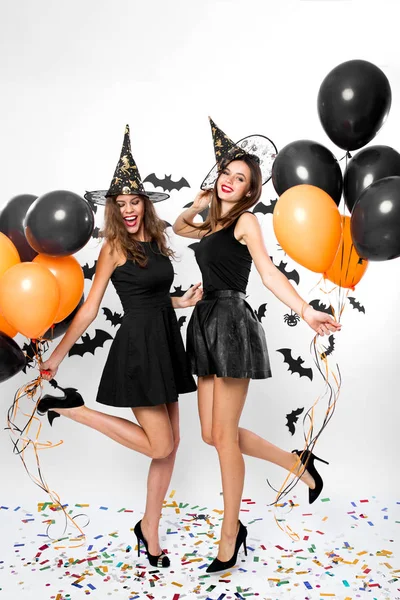 黒のドレスを着て 2 つの豪華な女性、魔女の帽子とハイヒール黒とオレンジ色の風船を保持します。ハロウィーン パーティー — ストック写真