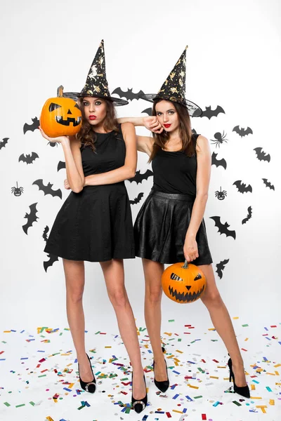 黒のドレスを着て 2 つの豪華な女の子魔女の帽子とハイヒールがコウモリで、背景にハロウィンのカボチャを保持 — ストック写真