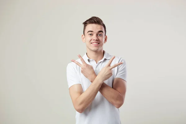 Happy guy habillé d'un t-shirt blanc et un jean montre signe V avec les deux mains sur un fond blanc dans le studio — Photo