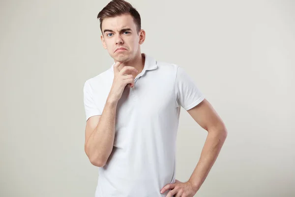 Cara pensativo vestido com uma camiseta branca e jeans está em um fundo branco no estúdio — Fotografia de Stock