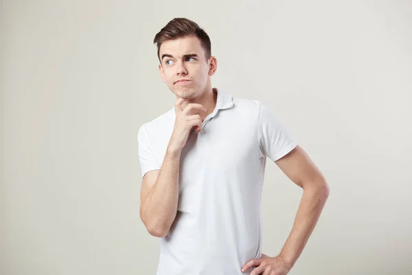 Cara pensativo vestido com uma camiseta branca e jeans está em um fundo branco no estúdio — Fotografia de Stock