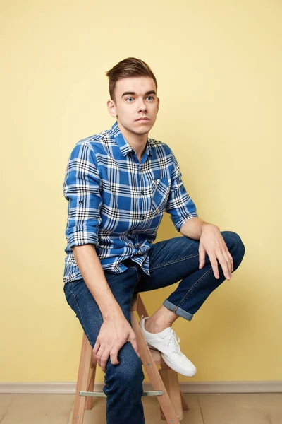 Mann in kariertem Hemd und Jeans sitzt auf einem Hocker vor gelbem Hintergrund im Studio — Stockfoto