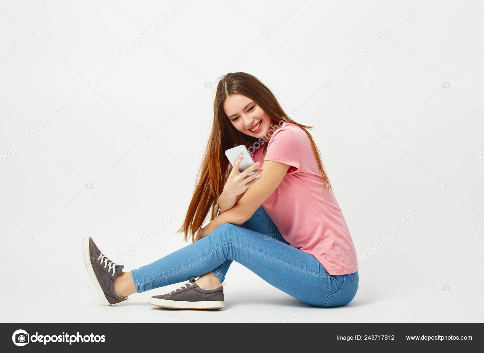 Beautiful girl dressed in a pink t-shirt, jeans and sneakers sits