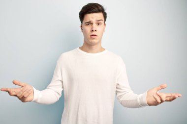 Sürpriz esmer adam giyinmiş bir beyaz uzun kollu beyaz bir arka plan üzerinde t-shirt ve jeans duruyor
