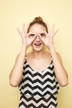 Çizgili bir üst ve beyaz kot giymiş kız yüz Studio sarı zemin üzerine onun parmaklarıyla işaret gözlük gibi gösterir