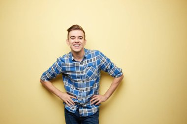 Nazik adam ekose gömlek ve kot pantolon giymiş stüdyoda sarı bir arka plan üzerinde oturuyor