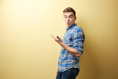 Bir ekose gömlek ve kot standları stüdyoda sarı duvar yanındaki şaşırmış adam giymiş