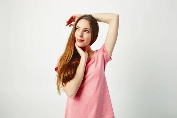 Menina de cabelos longos bonita vestida com uma camiseta rosa está em um fundo branco no estúdio — Fotografia de Stock