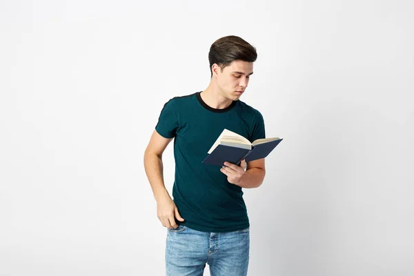Homme aux cheveux foncés vêtu d'un t-shirt et d'un jean vert foncé lit un livre sur fond blanc dans le studio — Photo