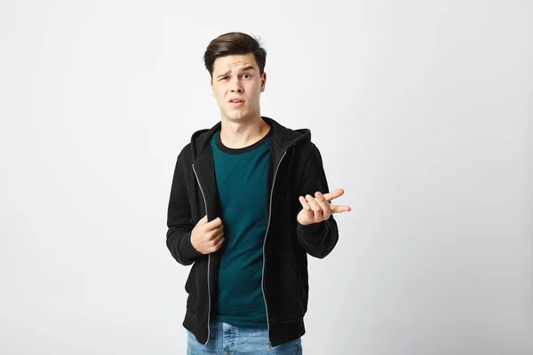 Cara engraçada vestida com uma camiseta verde escura, jeans e sweatshirt fica no estúdio em um fundo branco — Fotografia de Stock