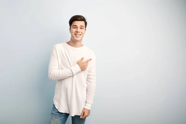 Sorrindo cara de cabelos escuros vestido com uma t-shirt manga comprida branca e jeans fica em um fundo branco — Fotografia de Stock