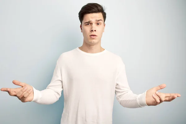 Surpreendido cara de cabelos escuros vestido com uma t-shirt manga comprida branca e jeans fica em um fundo branco — Fotografia de Stock