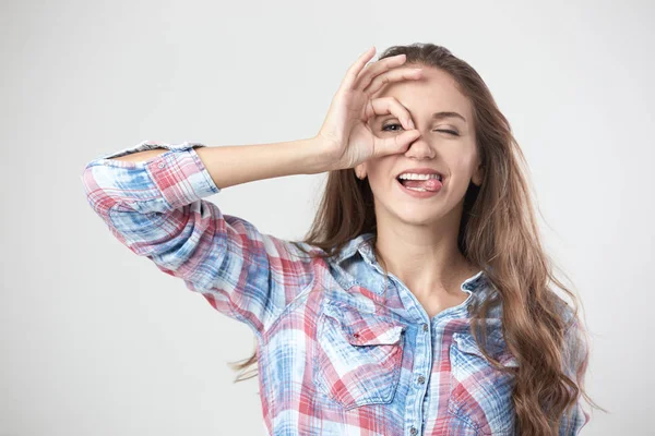 Rolig tjej visar tecken ok med fingrarna på hennes ansikte på den vita bakgrunden i studion — Stockfoto