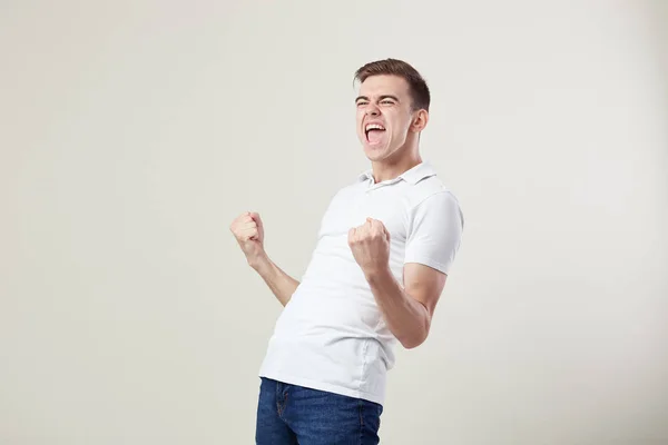 Full av energi glada kille klädd i en vit t-shirt och jeans lyckligt ropar i studion på en vit bakgrund — Stockfoto