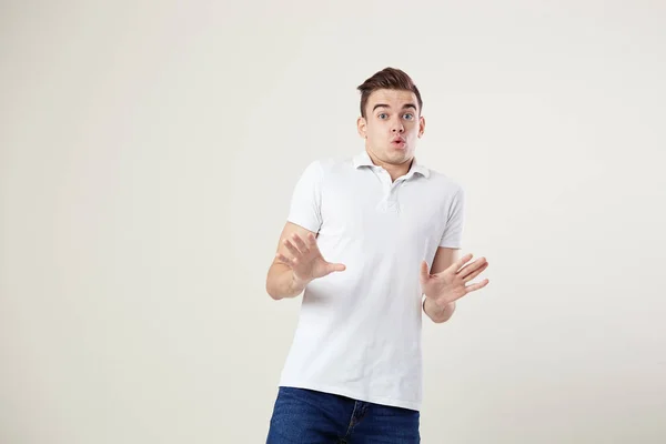 Querendo saber cara vestido com uma camiseta branca e jeans está em um fundo branco no estúdio — Fotografia de Stock