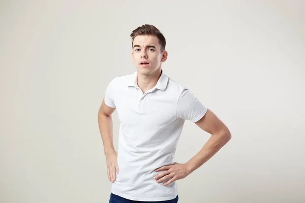 白い t シャツとジーンズに身を包んだナイスガイがスタジオで白い背景の上の腰に手を保持します。 — ストック写真