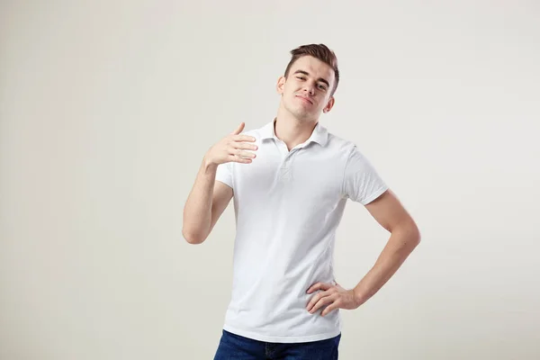 Cara indiferente vestido com uma camiseta branca e jeans está em um fundo branco no estúdio — Fotografia de Stock