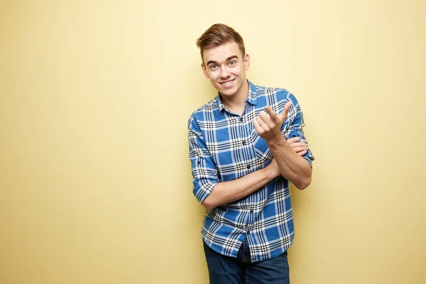 Cara alegre vestido com uma camisa xadrez e jeans fica ao lado da parede amarela no estúdio — Fotografia de Stock