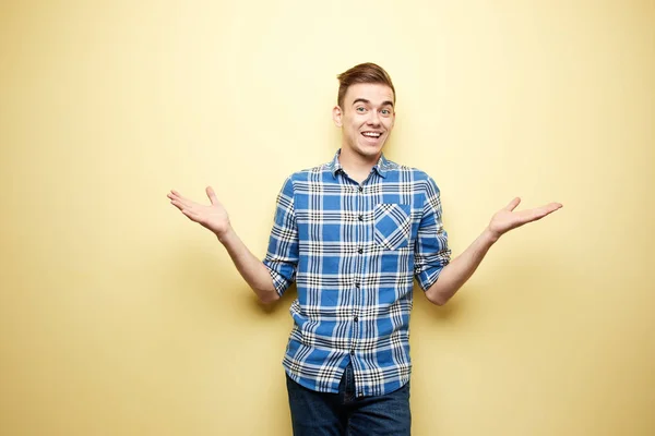 Cara alegre vestido com uma camisa xadrez e jeans fica ao lado da parede amarela no estúdio — Fotografia de Stock