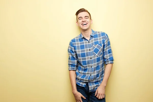 Cara alegre vestido com uma camisa xadrez e jeans fica ao lado da parede amarela no estúdio — Fotografia de Stock