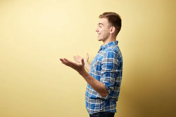 Удивленный парень в клетчатой рубашке и джинсах стоит рядом с желтой стеной в студии — стоковое фото