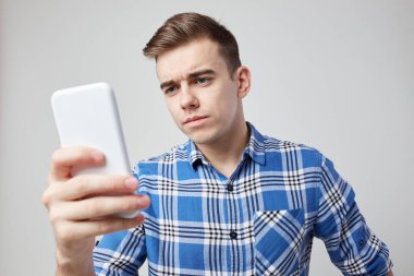 Bir ekose gömlek giymiş bir adam cidden cep telefonunu stüdyoda beyaz bir arka plan üzerinde görünüyor