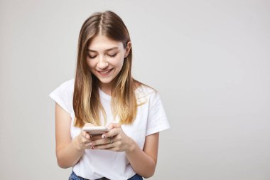 Mutlu kız içinde beyaz bir t-shirt gülümsüyor giyinmiş ve stüdyoda beyaz bir arka plan üzerinde cep telefonu kullanır