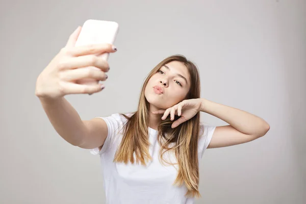 Chica feliz vestida con una camiseta blanca hace selfie sobre un fondo blanco en el estudio — Foto de Stock